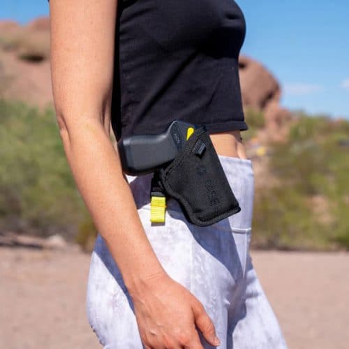 Person carrying a black stun gun holster outdoors, wearing a black top and white pants.