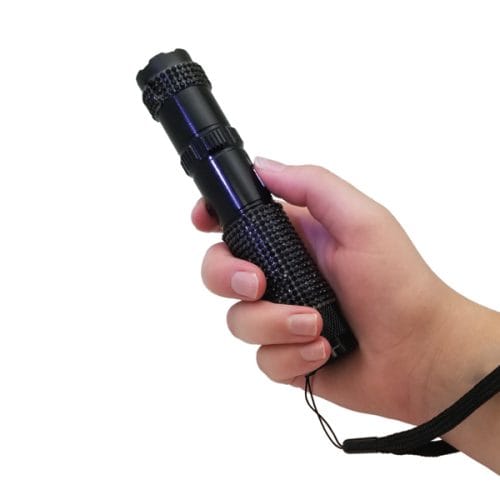 Hand holding a black tactical flashlight with wrist strap, isolated on white background.