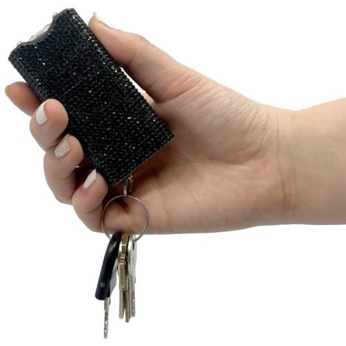 Hand holding a black rhinestone-covered stun gun with keys attached, showcasing compact self-defense tool.