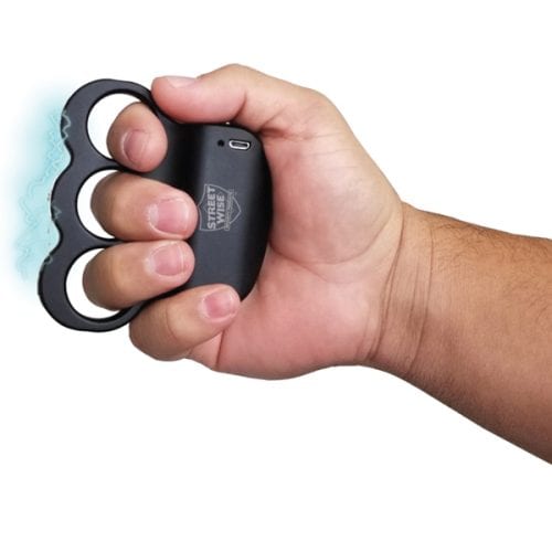 Person holding a black stun gun with built-in knuckles, designed for self-defense.