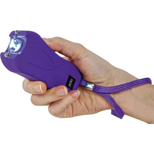 Purple stun gun with wrist strap held in hand, emitting a bright electric arc.