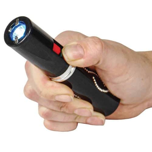 Hand holding a black stun gun with a bright LED light on, highlighting a close-up view of the device in action.