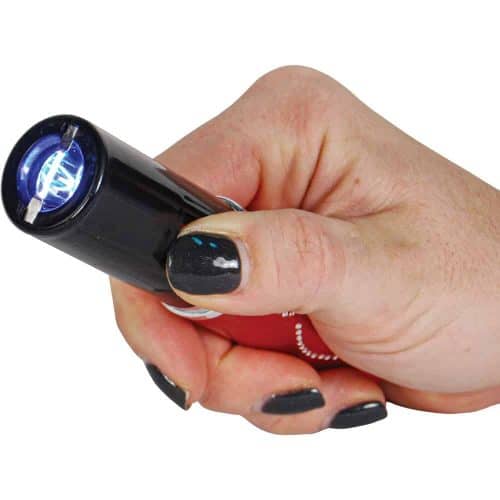 Hand holding a small black flashlight with a bright LED bulb turned on.